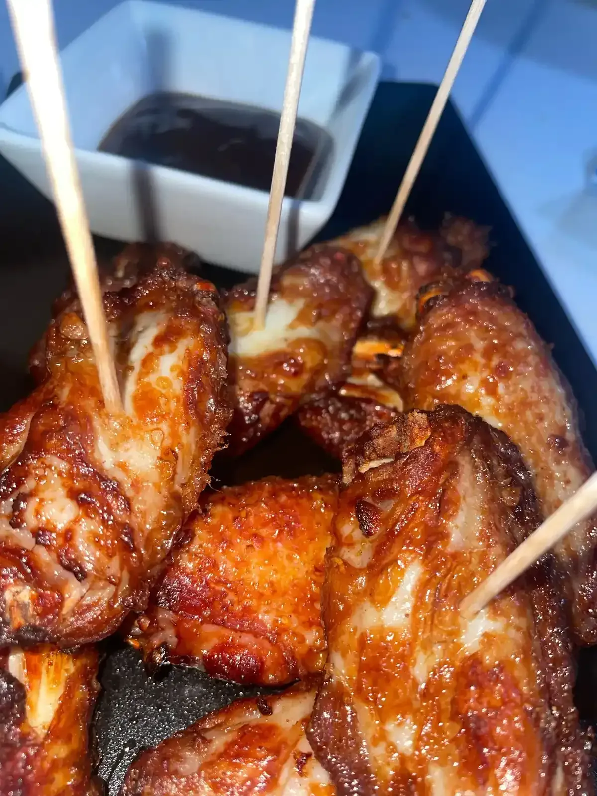 Primer plano de alitas de pollo doradas con palillos, servidas con un pequeño cuenco de salsa.