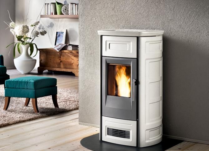 In einem Wohnzimmer steht ein weißer Ofen neben einem blauen Ottomanen.