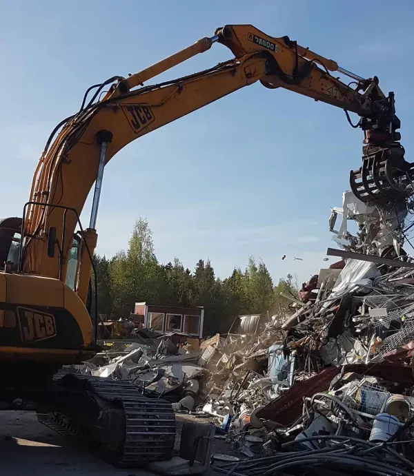 Keltainen JCB-kaivinkone purkaa rakennusjätettä.