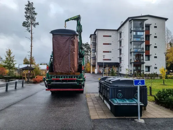 Roska-auto nostaa molokia kerrostalojen lähellä pilvisenä päivänä.