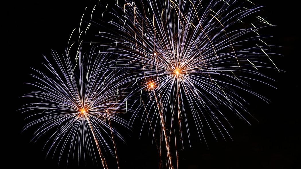 Feuerwerkskörper explodieren am Nachthimmel mit weißen und orangen Farbtupfern.