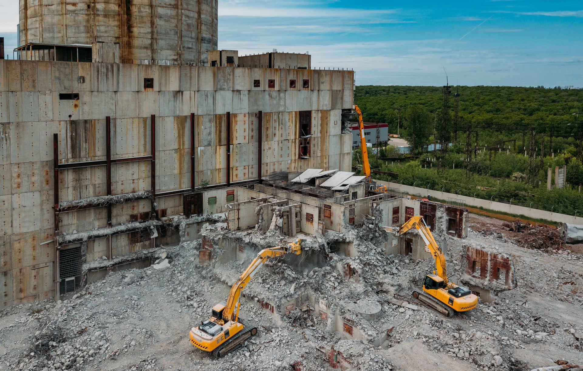 Deux pelleteuses jaunes démolissent un bâtiment industriel.