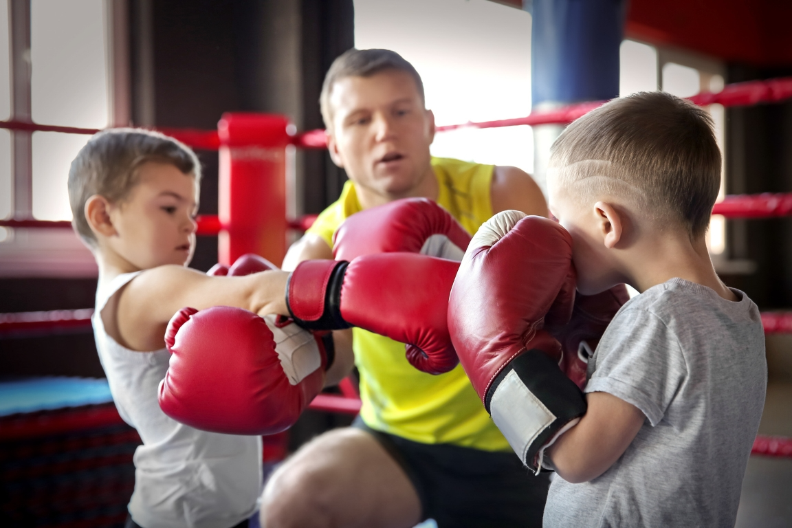 A man is teaching two young boys how to box in a boxing ring.