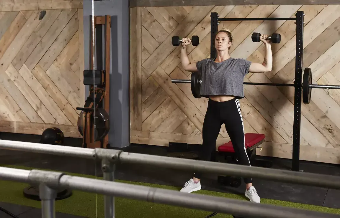 A woman is lifting dumbbells in a gym.