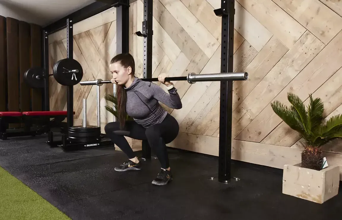 A woman is squatting with a barbell in a gym.
