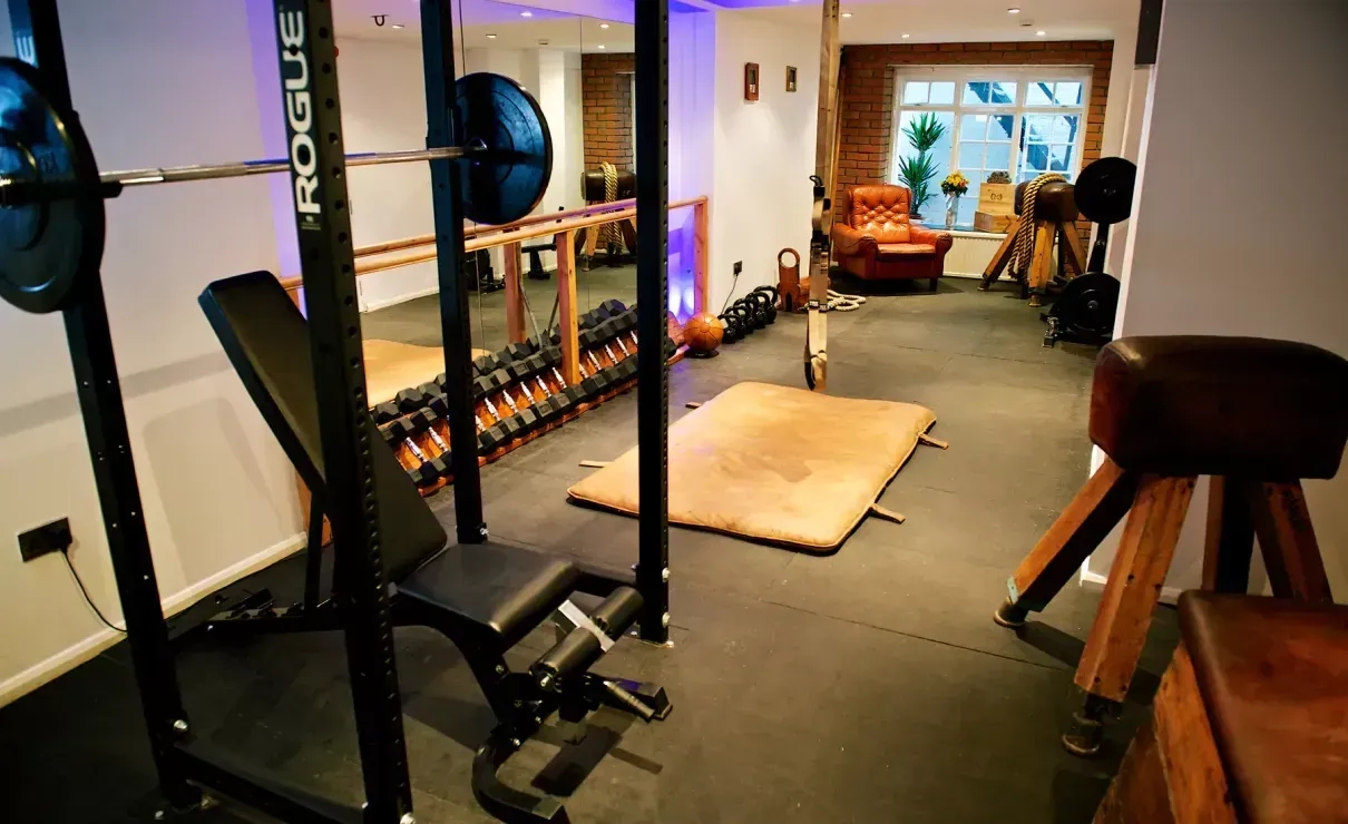 A gym with a bench , squat rack , dumbbells , and a stool.