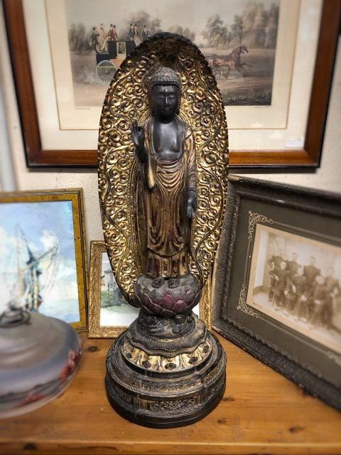 Statue de Bouddha  sombre avec dorure sur un meuble en bois avec des photos et tableaux autour