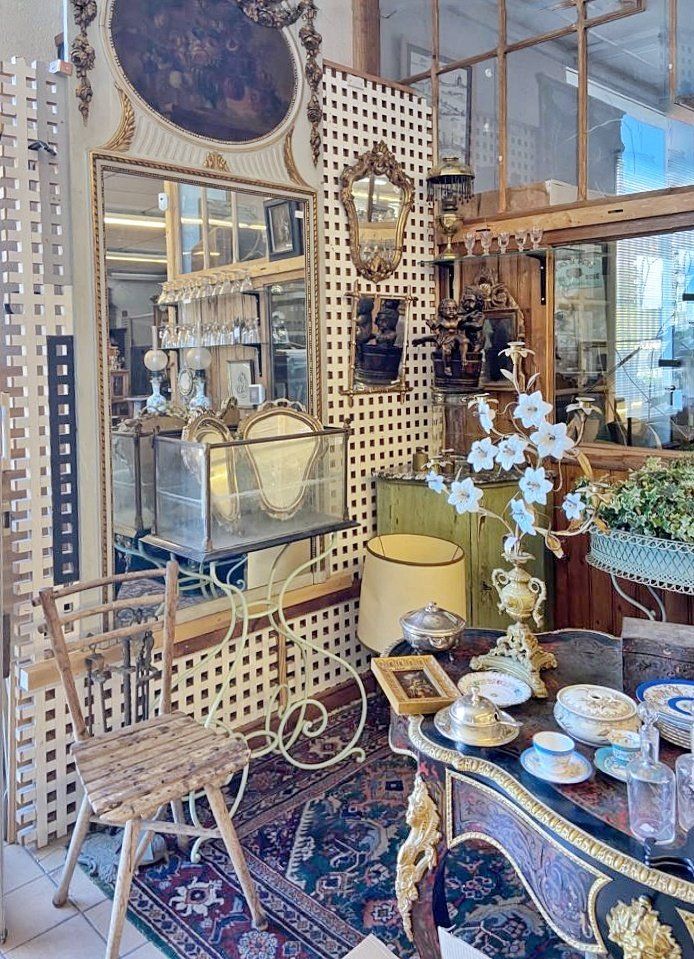 Espace chez un antiquaire proposant une chaise en bois à gauche, un miroir et un tableau rond au dessus, une table à droite