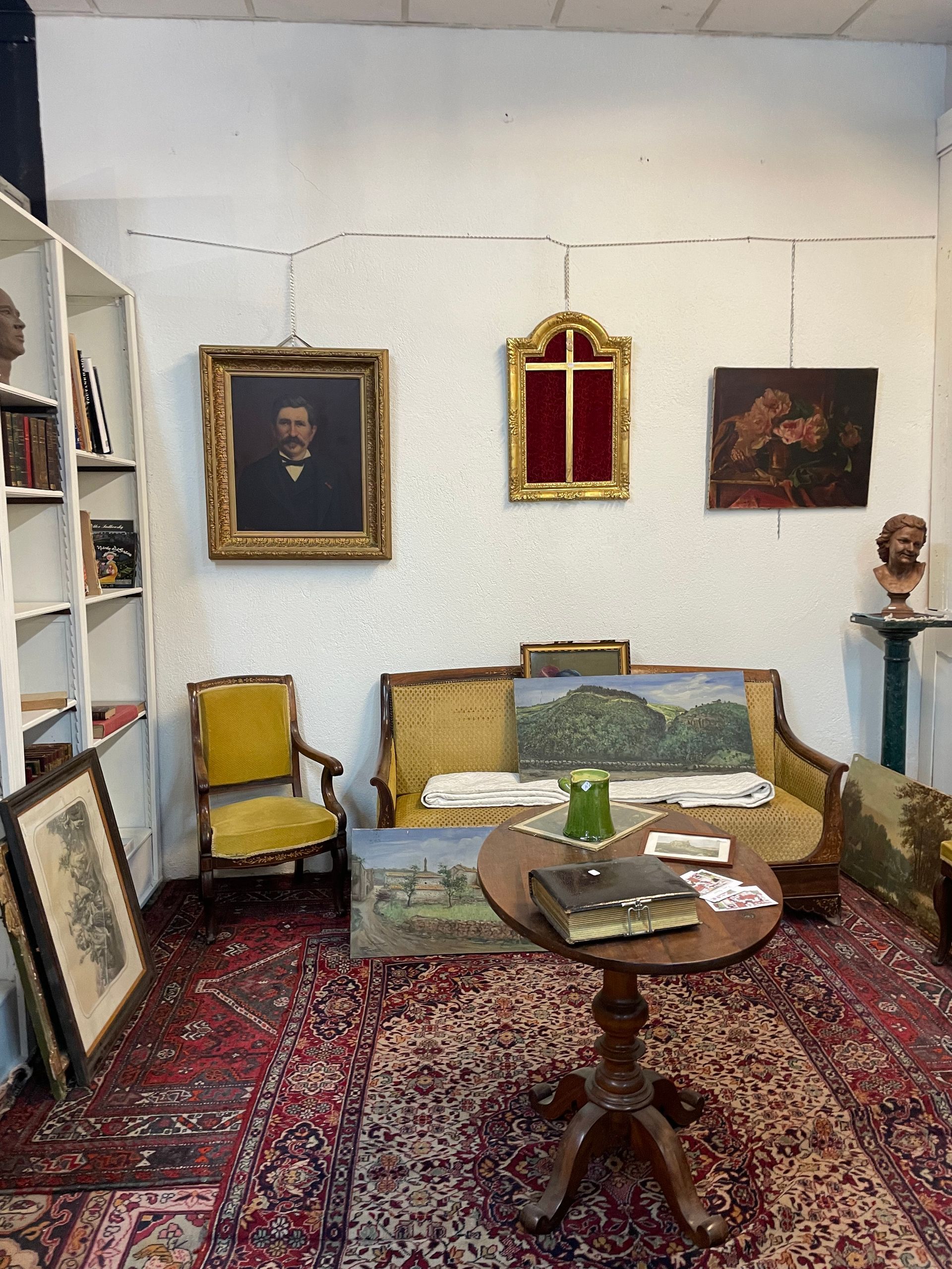 Un salon d'antiquaire avec une chaise à gauche, un canapé assorti au milieu, et des tableaux au mur derrière