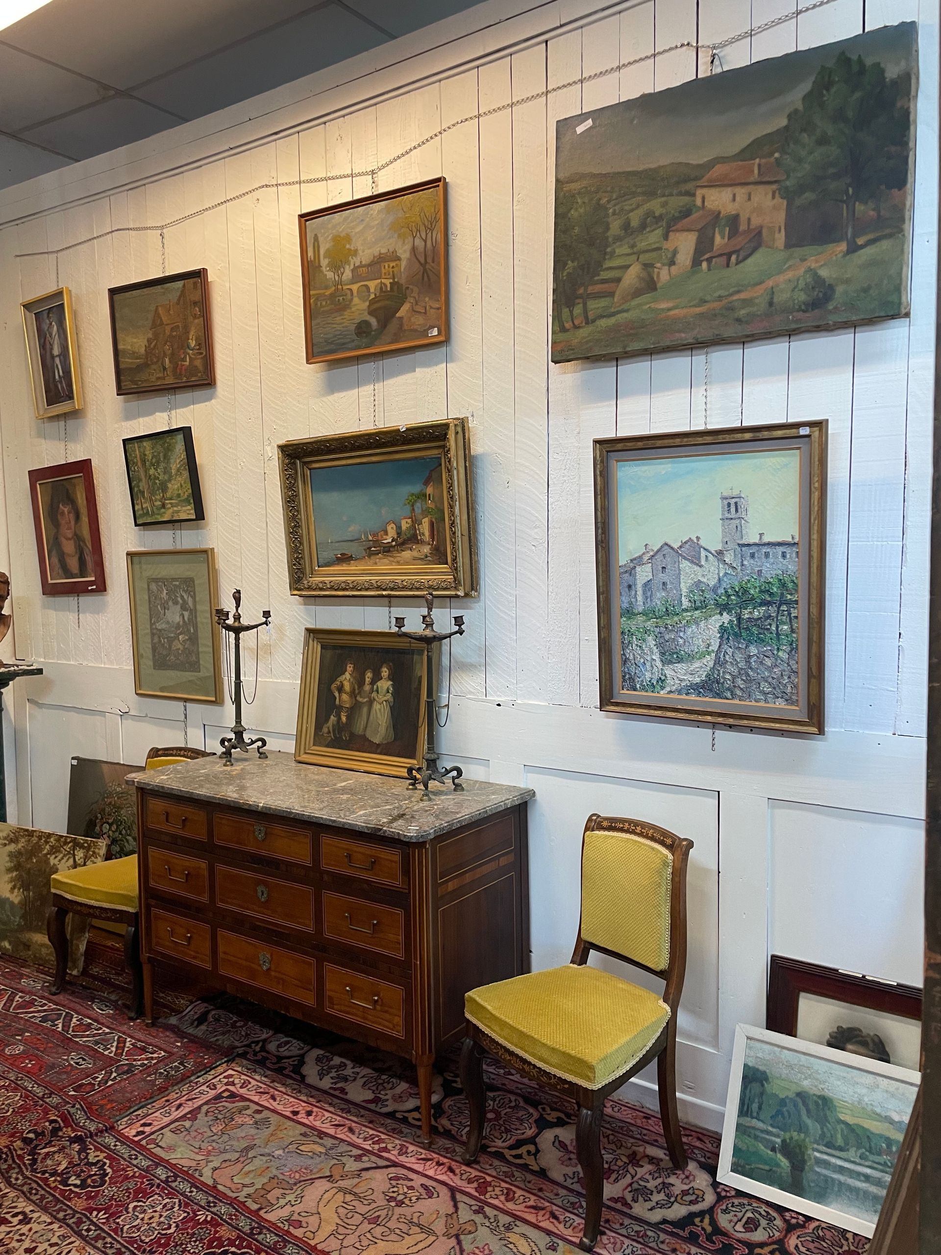 Des tableaux au mur d'un antiquaire et un meuble en bois avec tableau et chandeliers dessus