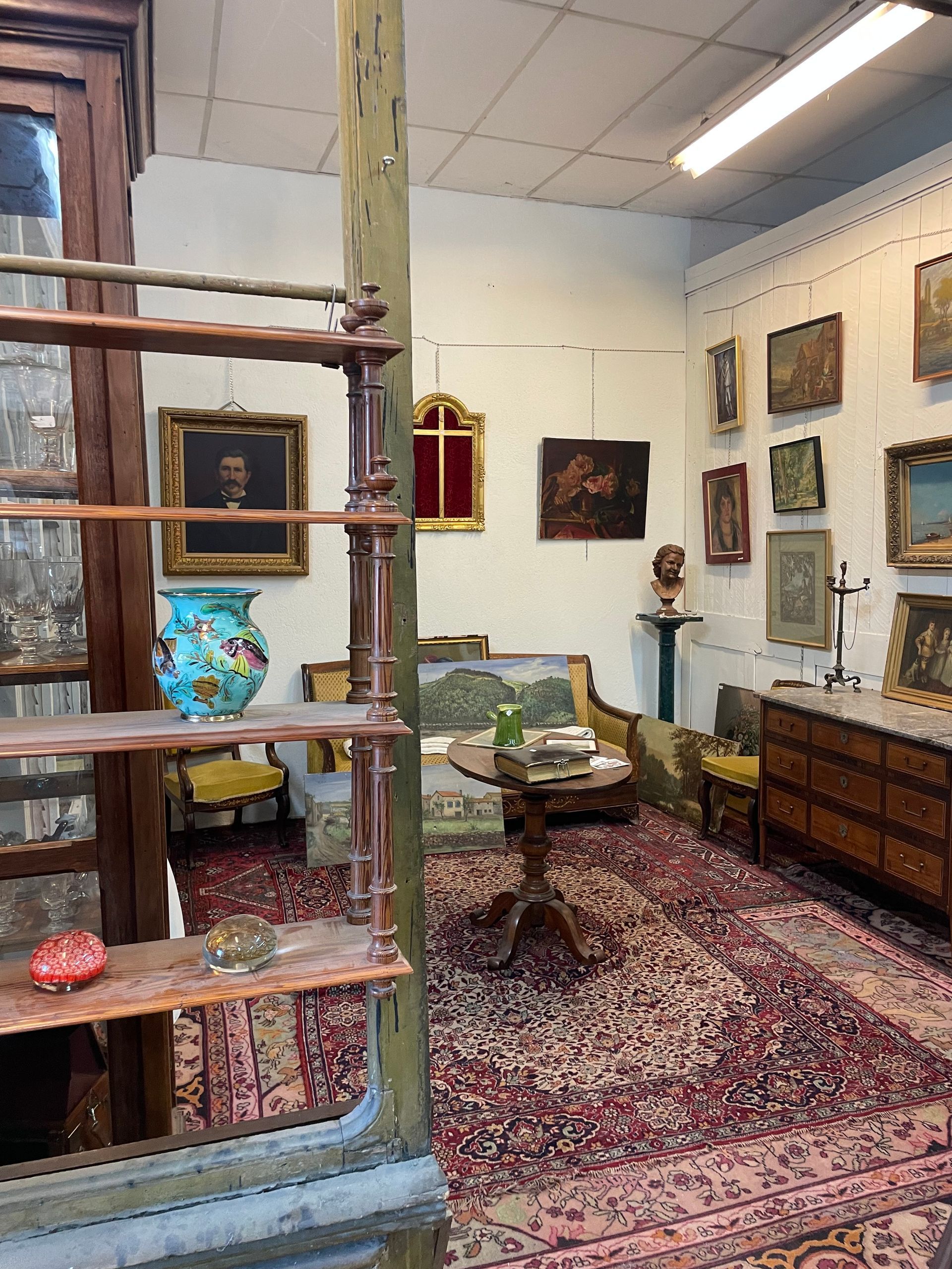 Une étagère vide à gauche, et au centre un espace avec tapis, table basse, canapé, fauteuils et tableaux au mur