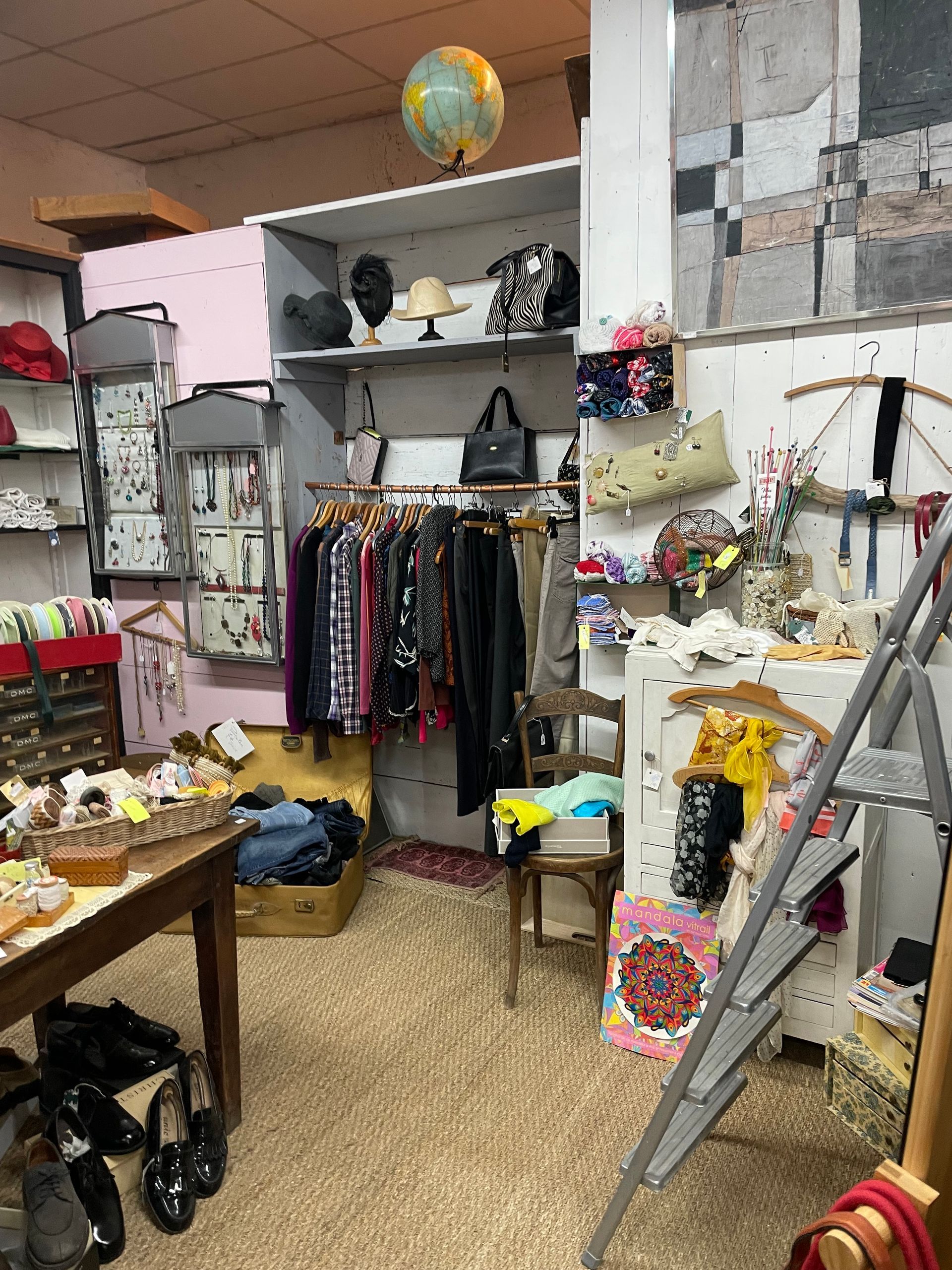 Une penderie dans l'espace de mercerie d'un antiquaire avec des bijoux à gauche, des chapeaux en haut, et un escabeau à droite