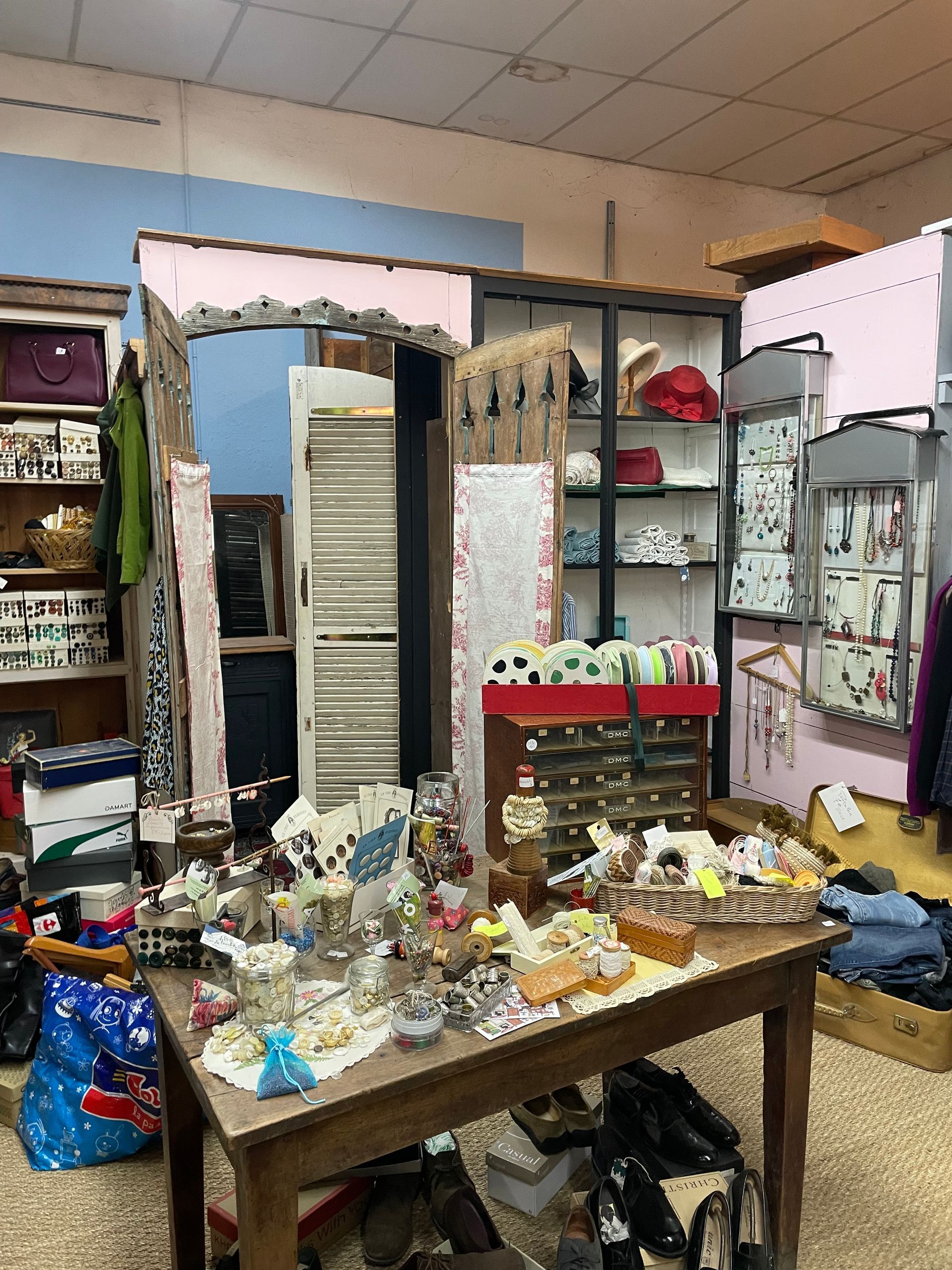 L'espace mercerie d'un antiquaire présentant divers ustensiles sur une table au centre, des bobines de fil, des bijoux