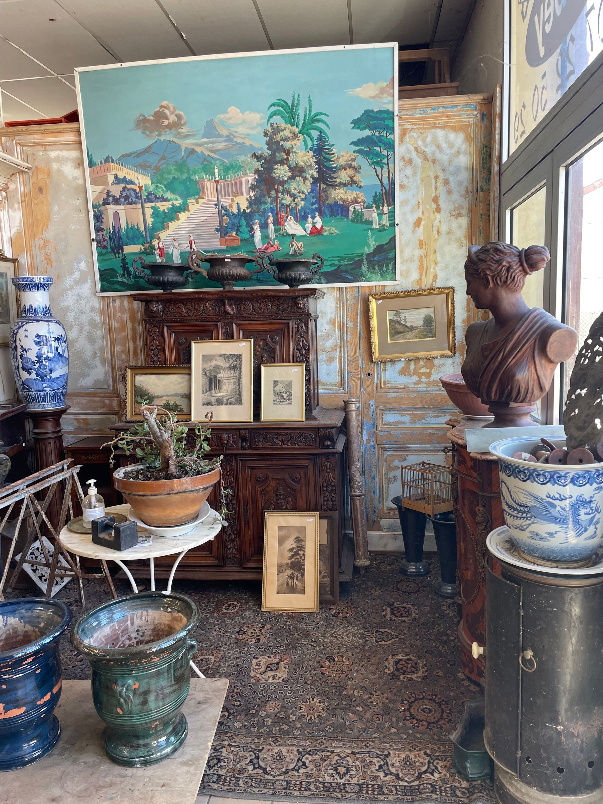Boutique de l'antiquaire avec de gauche à droite un pot, un buste de femme, des tableaux, un meuble, une table, un pot