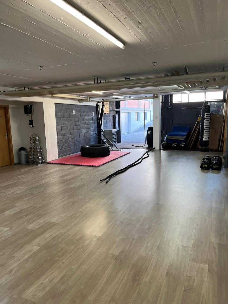 Vue grand angle de l'intérieur d'une salle de sport avec un parquet clair, un tapis rouge central.