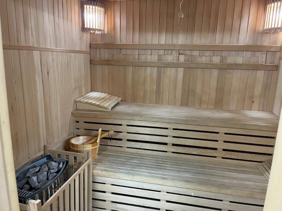Vue intérieure d'un sauna avec des murs en bois, des banquettes étagées, un poêle à pierres et un seau en bois.