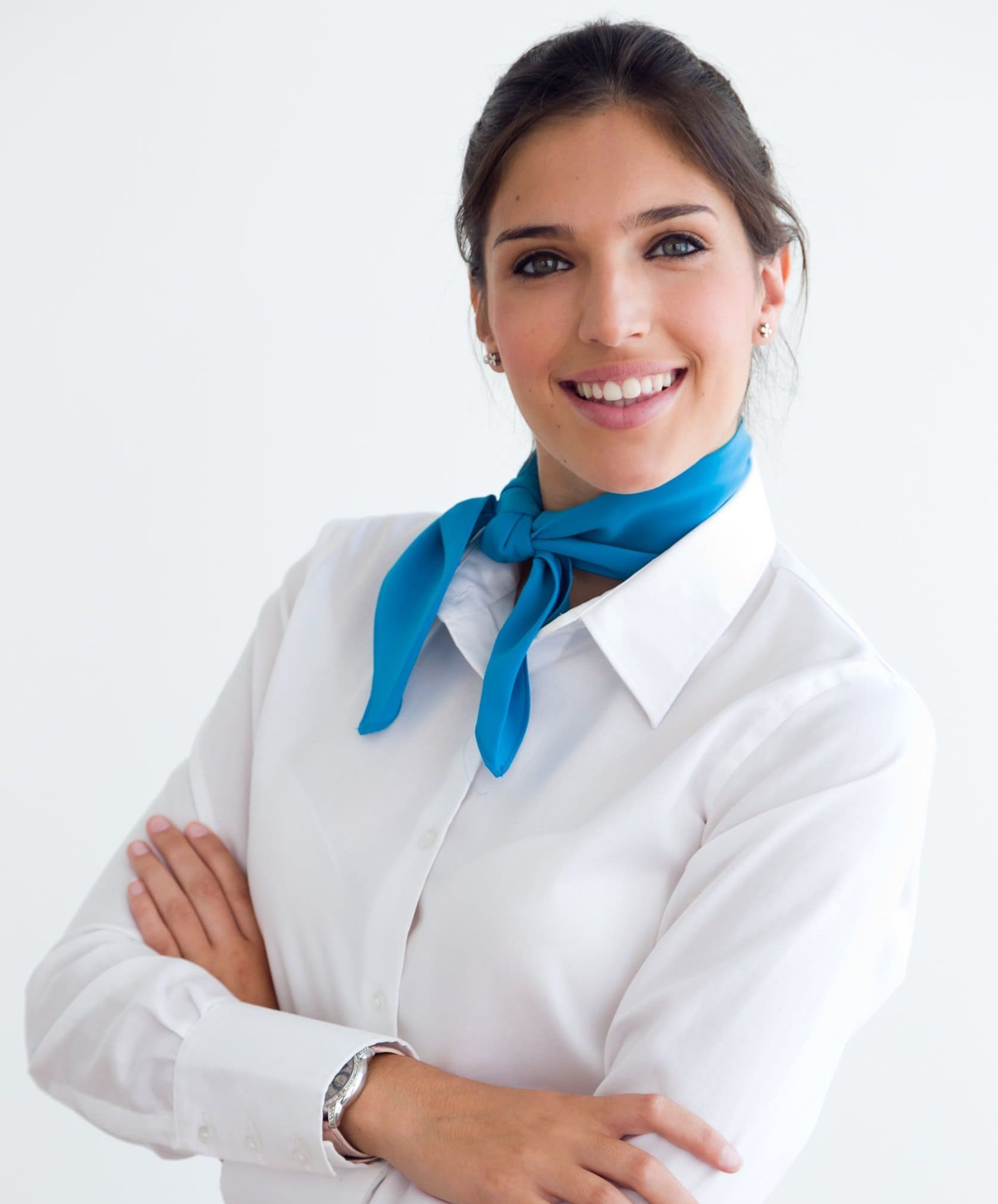 Una mujer vestida con una camisa blanca y una bufanda azul sonríe con los brazos cruzados.