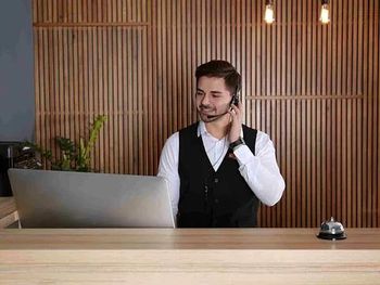 Un hombre está sentado en un escritorio con una computadora portátil y hablando por un auricular.