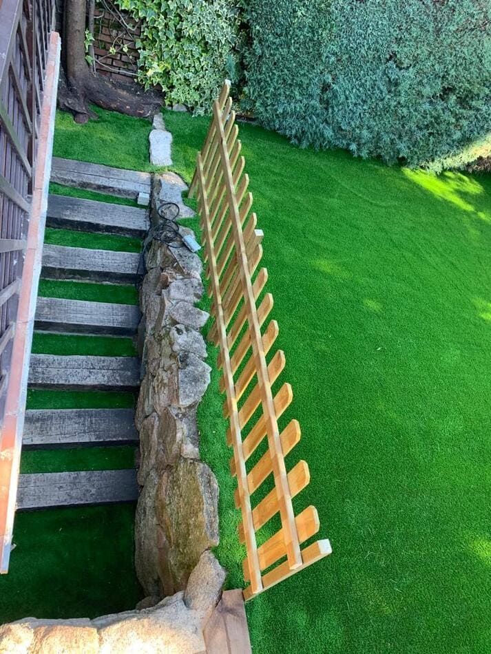 Una valla de madera se encuentra encima de un exuberante césped verde al lado de unas escaleras.