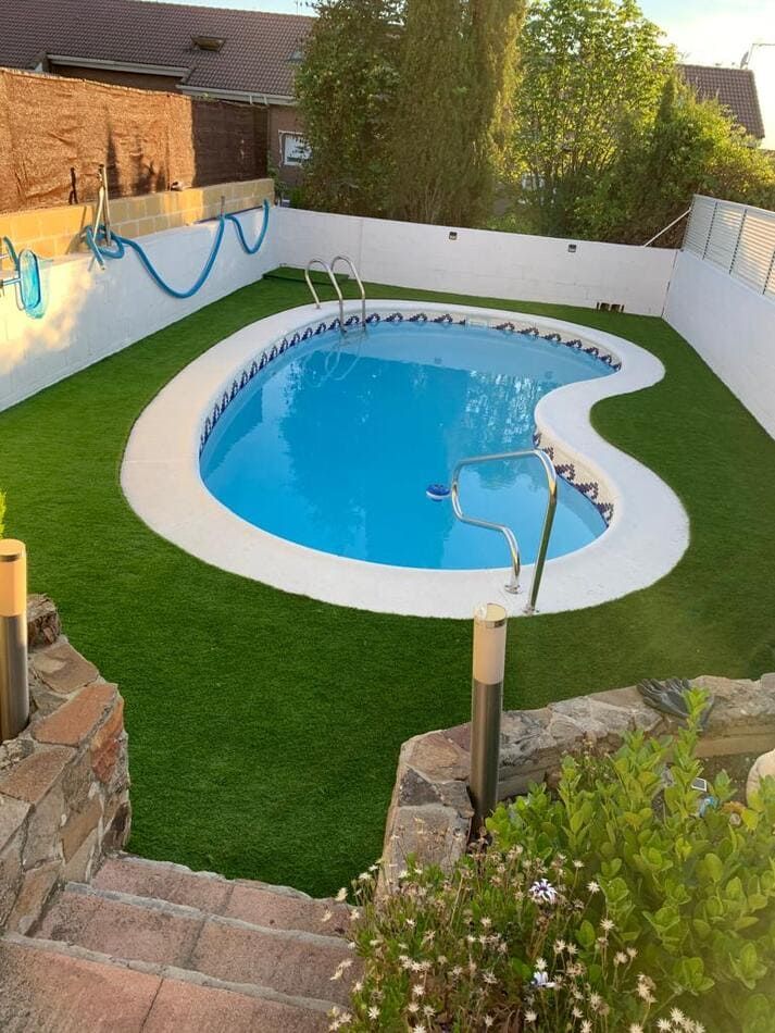 Una gran piscina rodeada de una valla blanca y césped.