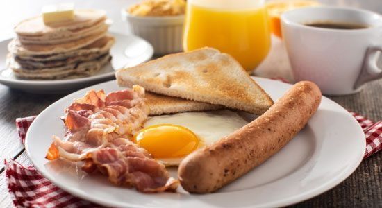 Plato de desayuno con huevo, tocino, salchicha, tostadas, panqueques, jugo y café.