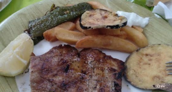 Carne a la parrilla, patatas, verduras y limón en un plato.