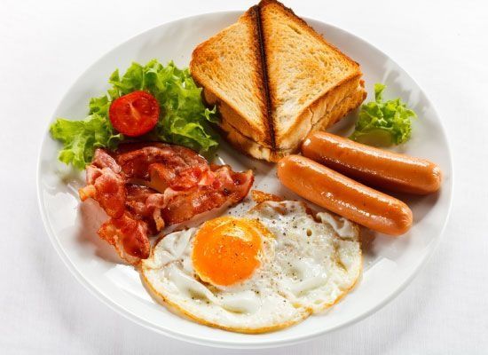 Plato de desayuno: huevo frito, tocino, salchichas, sándwich tostado, tomate y lechuga.