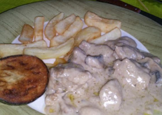 Plato de comida: pollo en salsa cremosa, patatas gajo y una rodaja de berenjena frita.