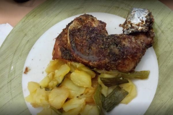 Plato de pollo asado con patatas y verduras verdes.