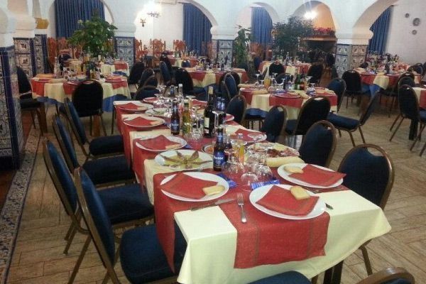 Interior de restaurante con mesas preparadas para comer. Las mesas tienen caminos rojos, sillas azules y platos con comida.