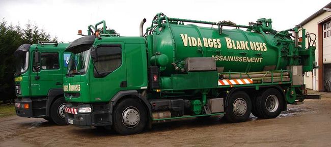 Deux camions aspirateurs verts garés côte à côte dans une cour boueuse, avec le nom de l’entreprise inscrit en blanc.