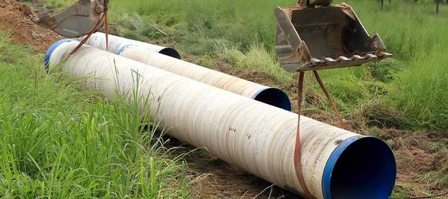 Gros tuyau blanc aux extrémités bleues posé dans l’herbe à côté du godet d’une excavatrice
