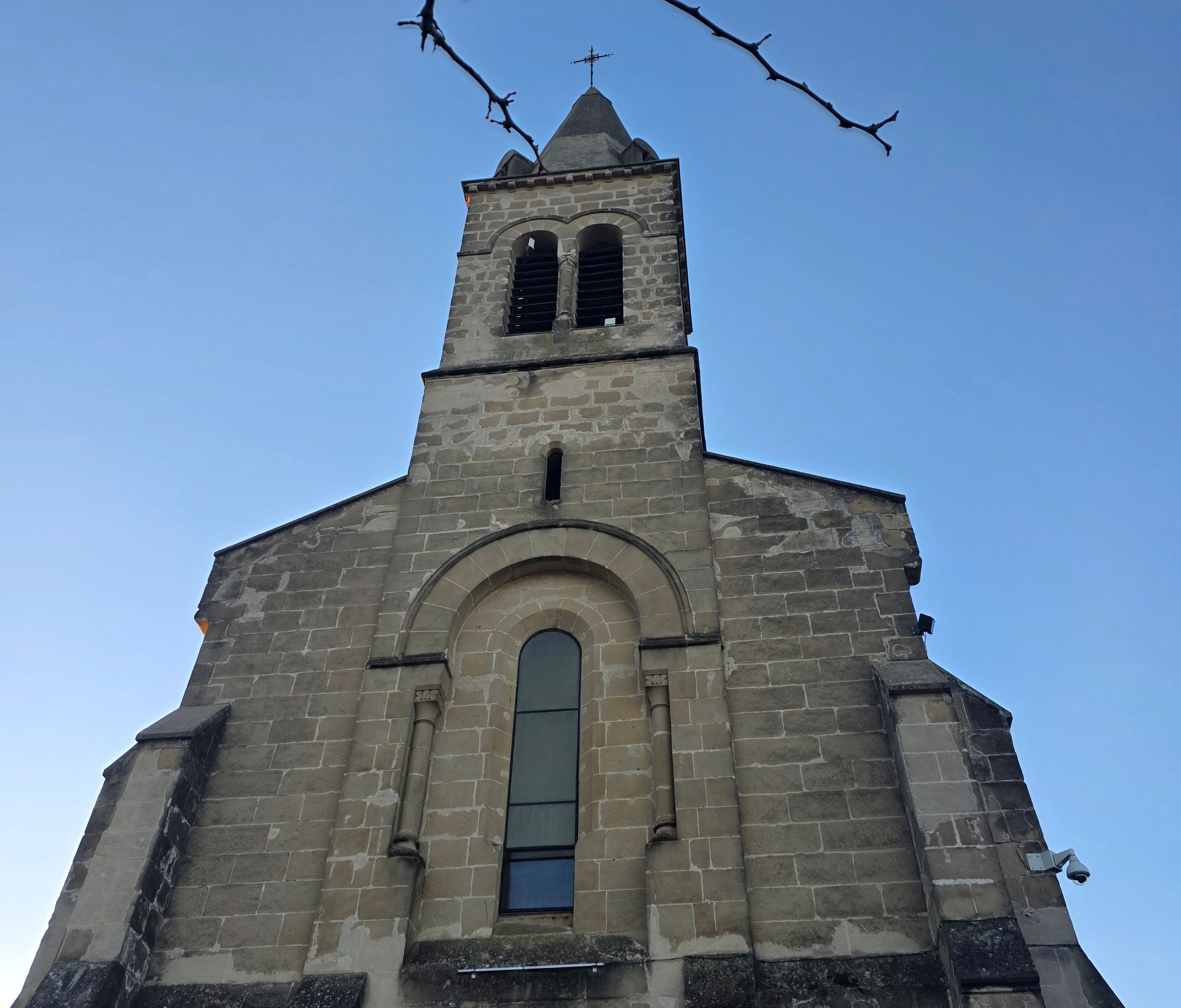 Église en pierre avec clocher, branche d'arbre dans le coin supérieur droit.