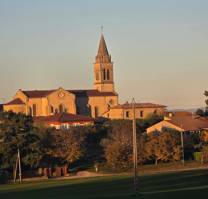 Église au clocher, entourée de bâtiments et d'arbres.