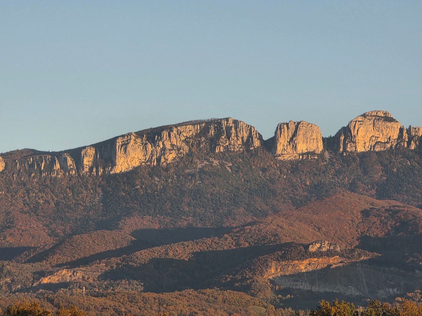 Chaîne de montagnes sous un ciel bleu limpide, baignée par un soleil chaud.