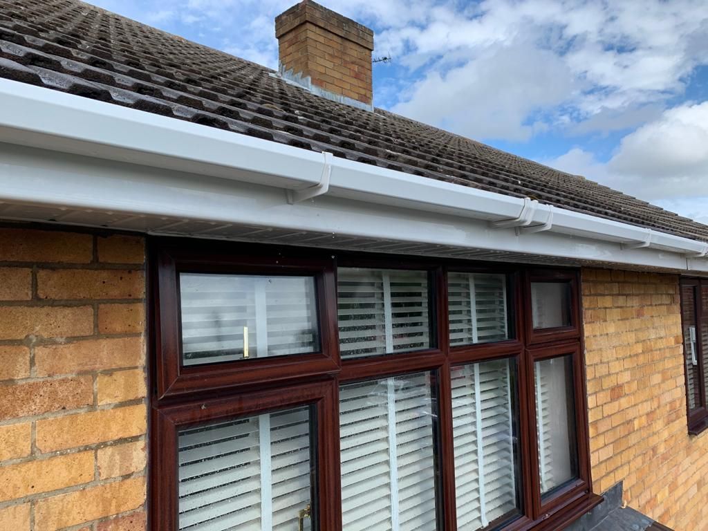 Brick house window with white shutters and dark brown trim beneath a tiled roof and cloudy sky