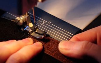 Primer plano de unas manos cosiendo una cremallera marrón a una tela oscura utilizando una máquina de coser.