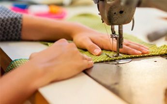 Manos cosiendo tela verde en una máquina de coser.