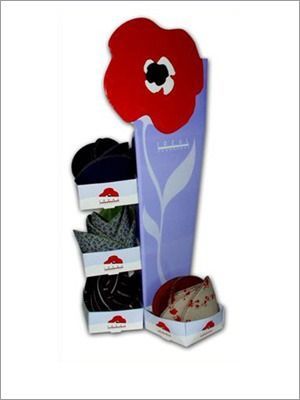Exhibición de sombreros en cajas de cartón, con diseño de flores rojas y fondo lavanda.