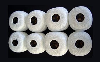 Ocho carretes de hilo blanco dispuestos muy juntos, sobre un fondo oscuro.