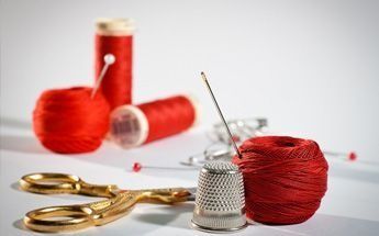 Herramientas de costura: carretes de hilo rojo, tijeras, dedal y alfileres.