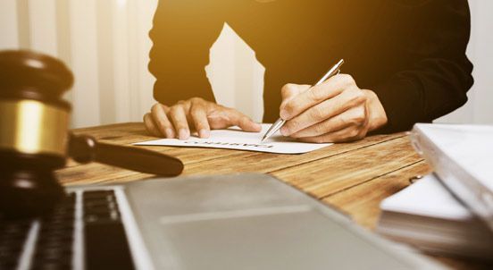 Una persona está sentada en una mesa escribiendo en un trozo de papel.
