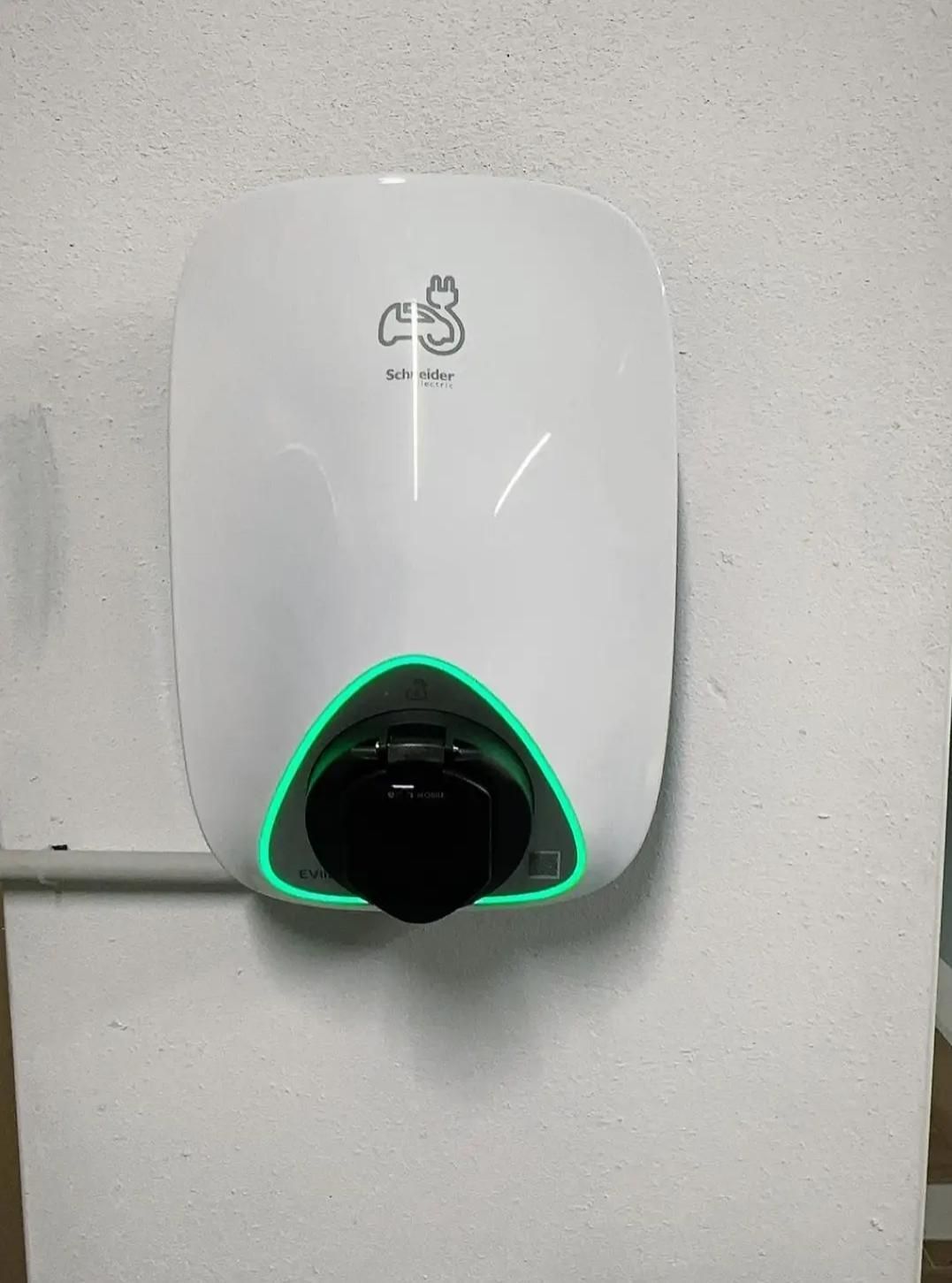 Une borne de recharge murale blanche pour véhicules électriques, ornée d'un logo et d'un anneau lumineux circulaire vert autour du port de charge.