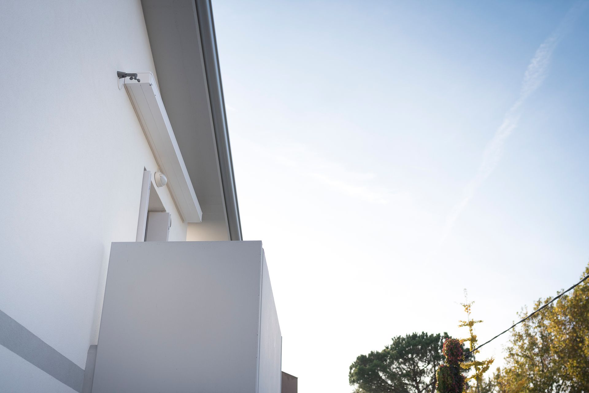 Una vista dal basso della facciata di un moderno edificio bianco con un piccolo balcone sotto un cielo azzurro e limpido.