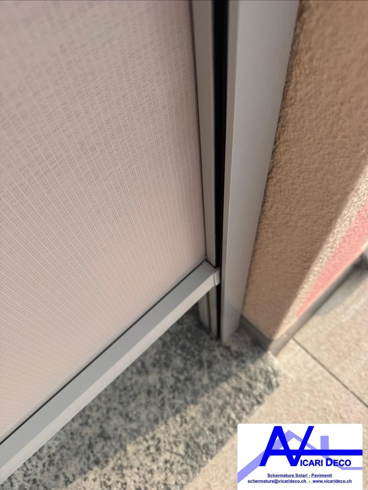 Vista ravvicinata di un pannello divisorio di colore chiaro installato su una parete con finitura a rilievo e cornice metallica.