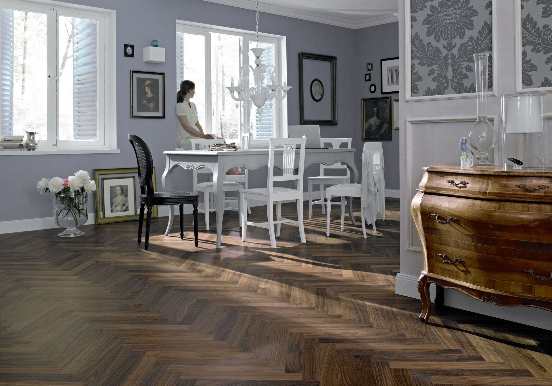 Sala da pranzo con pavimento in parquet a spina di pesce, tavolo bianco con sedie, pareti grigie e una cassapanca in legno vintage.