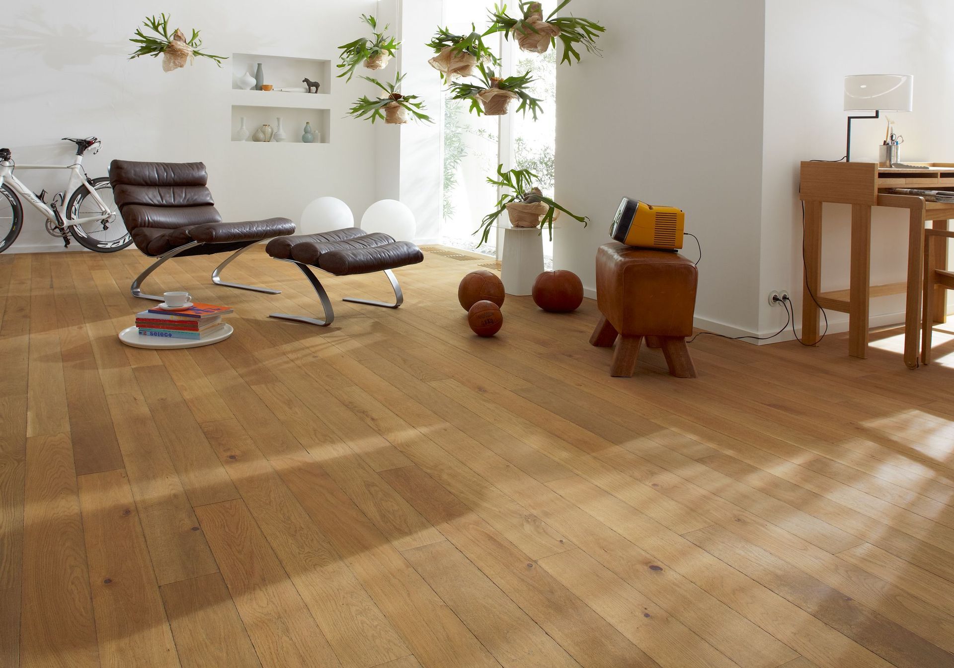 Un soggiorno moderno con pavimento in rovere, poltrona in pelle, piante in vaso e scrivania addossata a una parete bianca.