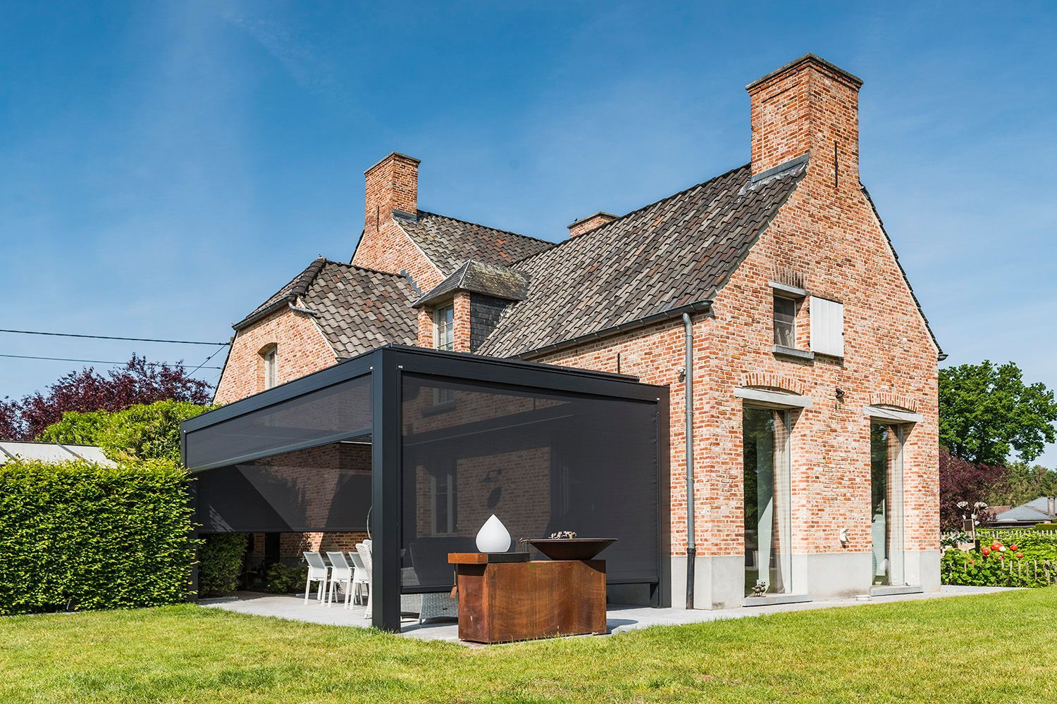 Una casa in mattoni con un pergolato scuro e moderno e schermi per la privacy retrattili annessi al patio posteriore.