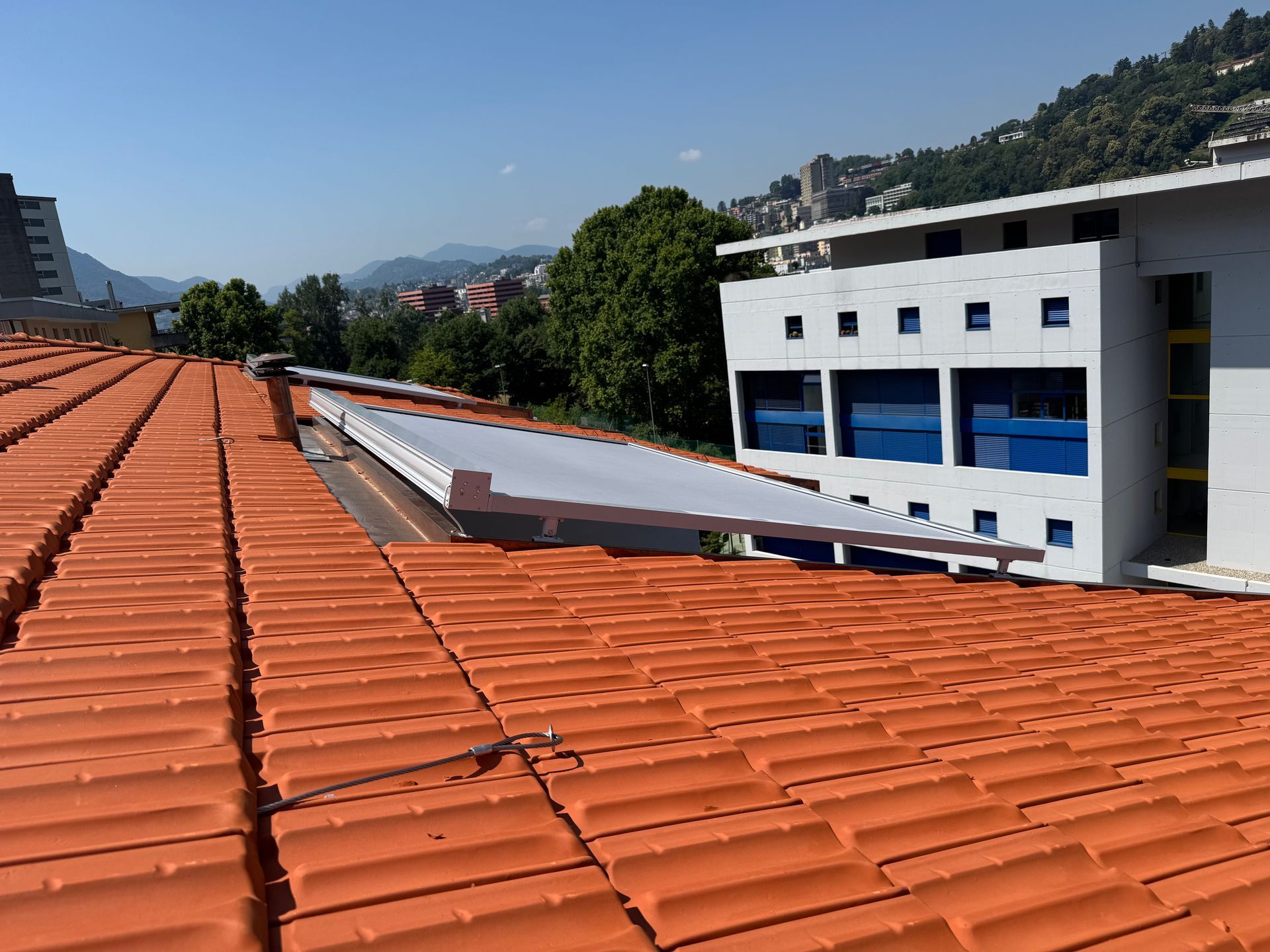 Un tetto di tegole arancioni brillanti, caratterizzato da un elemento architettonico moderno bianco che si estende verso un edificio bianco adiacente.