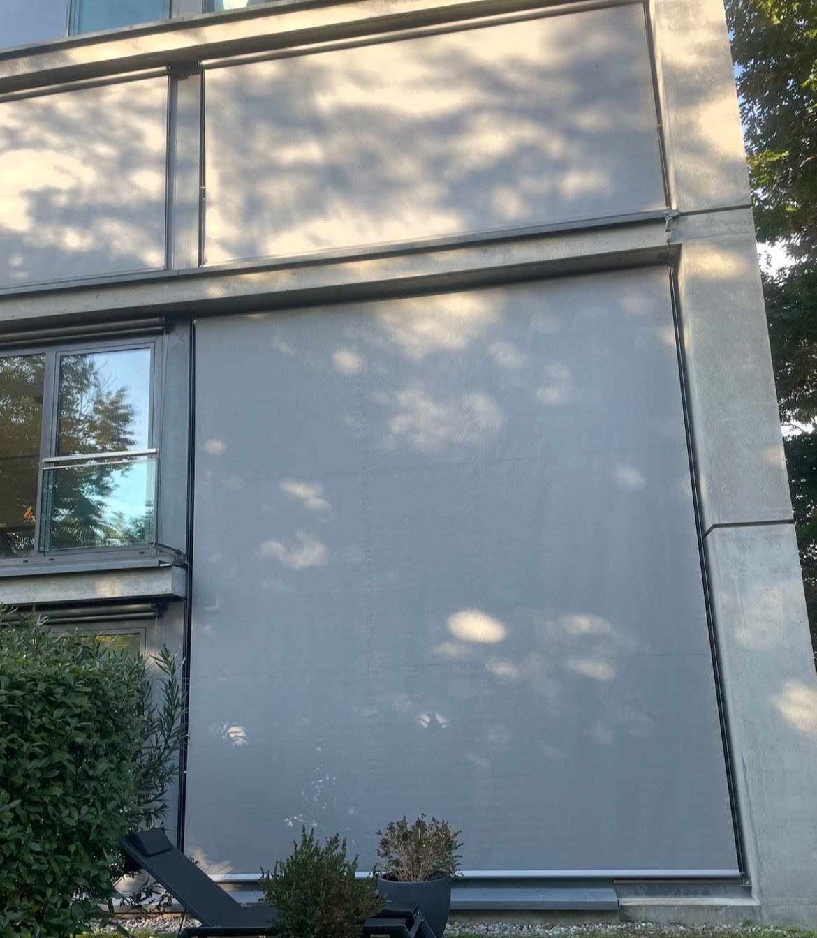 Tende parasole esterne di colore grigio chiaro che coprono le grandi vetrate della facciata di un moderno edificio in cemento.